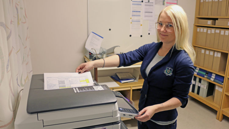 Blond kvinna med glasögon vid en kopieringsmaskin.