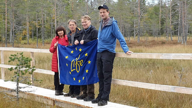 Tre män och en kvinna håller upp en EU-flagga framför sig.